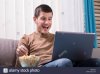 happy-young-man-watching-movie-on-laptop-and-eating-popcorn-at-home-M6GJH3.jpg